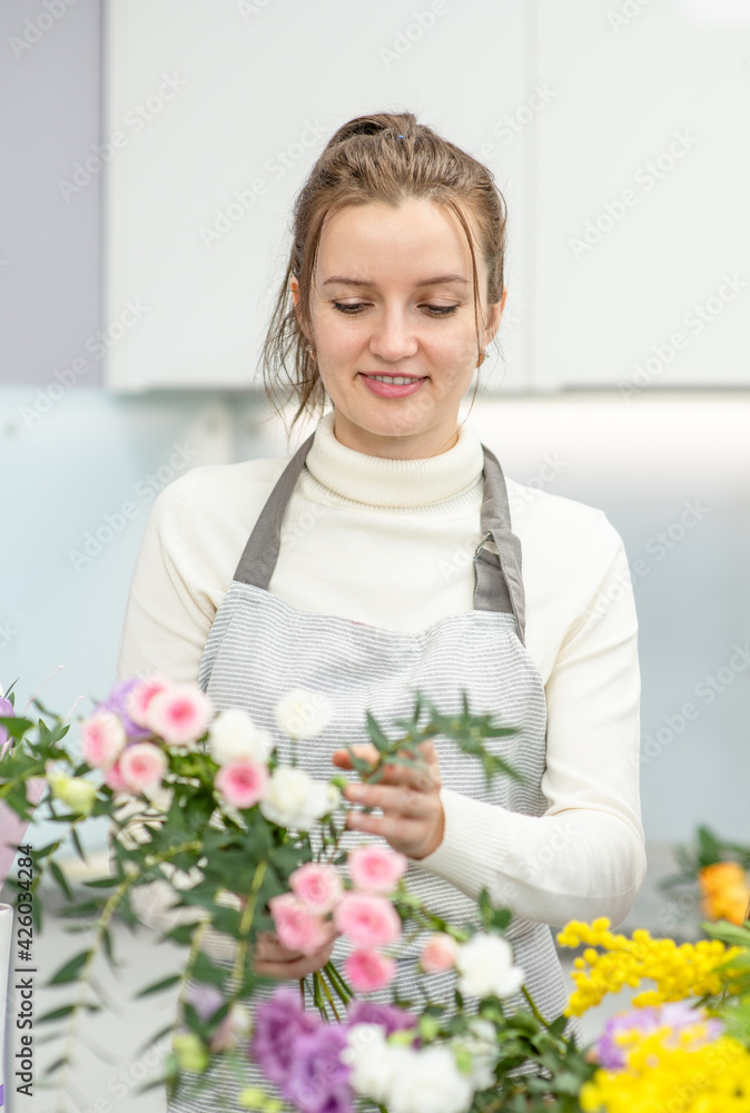 Florist wearing apron arranging a bouquet of beautiful colorful flowers inside her floral shop Florist wearing apron arranging a bouquet of beautiful colorful flowers inside her floral shop
