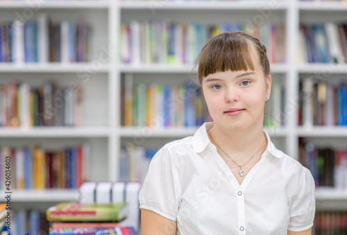 Portrait of a young girl with syndrome down at library. Empty space for text. Education for disabled children concept