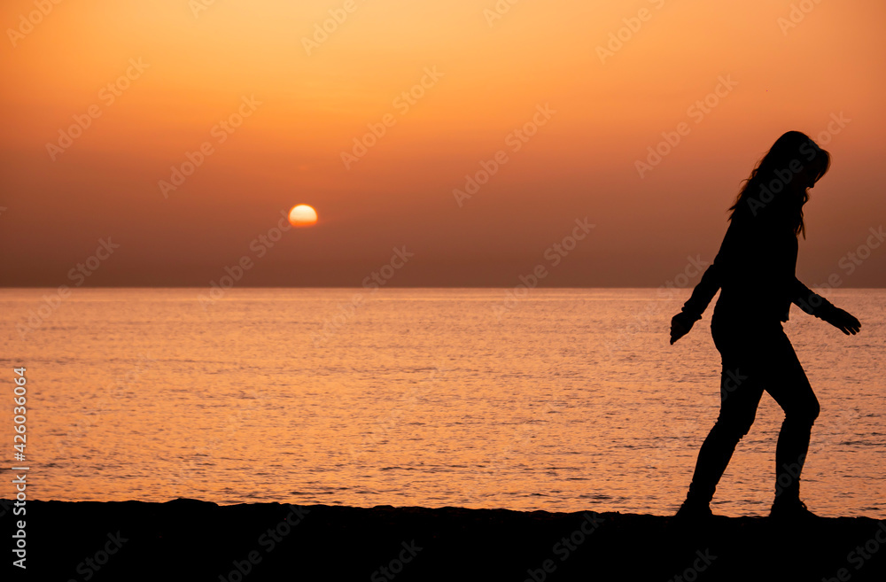 Silhouette of a woman walking by the ocean. Woman shilouette at sunrise on the beach