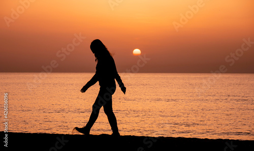 Silhouette of a woman walking by the ocean. Woman shilouette at sunrise on the beach © Robert