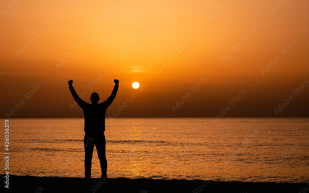 Silhouette of a man by the ocean. Man shilouette at sunrise on the beach.  Man with victory expression