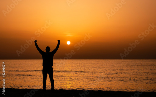 Silhouette of a man by the ocean. Man shilouette at sunrise on the beach.  Man with victory expression