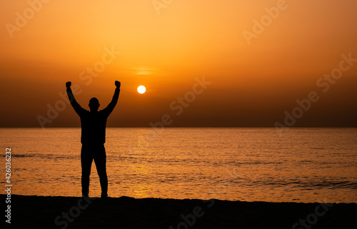 Silhouette of a man by the ocean. Man shilouette at sunrise on the beach.  Man with victory expression