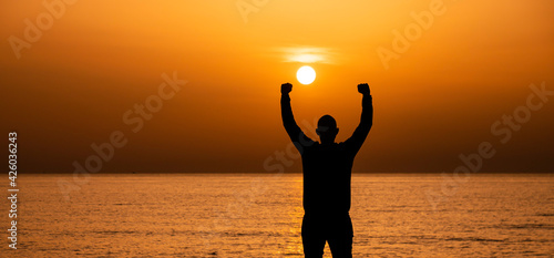 Silhouette of a man by the ocean. Man shilouette at sunrise on the beach.  Man with victory expression
