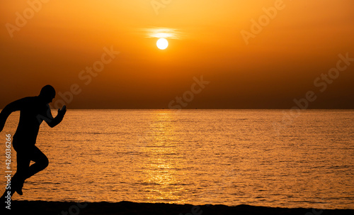 Silhouette of a man running by the ocean. Man shilouette at sunrise on the beach