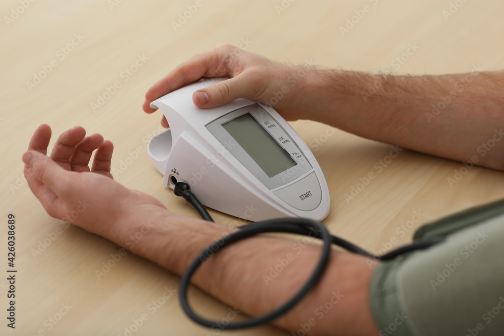 man checking blood pressure at wooden table indoors, closeup man checking blood pressure at wooden table indoors, closeup