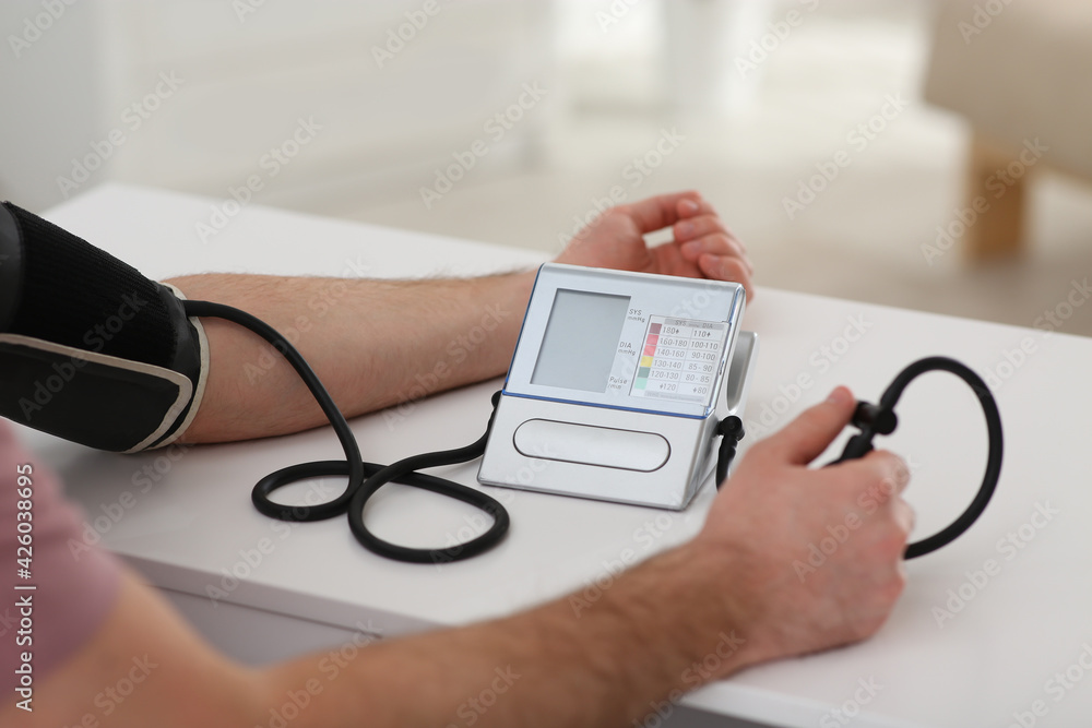 Man checking blood pressure at table indoors, closeup Man checking blood pressure at table indoors, closeup