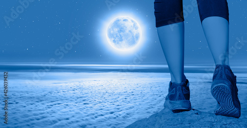 Woman walking (hiking) go up  a snowy mountain - Woman walking sport feet on trail healthy lifestyle fitness - Night sky with moon in the clouds 