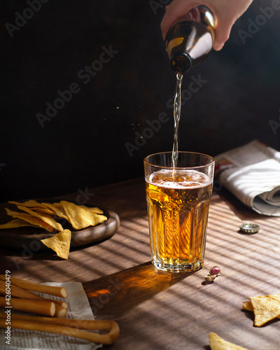 Hand pours light beer into glass, dark background