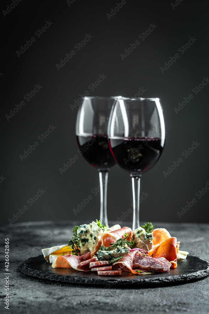 Italian antipasti wine snacks set. Cheese variety, janon, crudo, Prosciutto di Parma, salami and wine in glasses on dark background - obrazy, fototapety, plakaty 