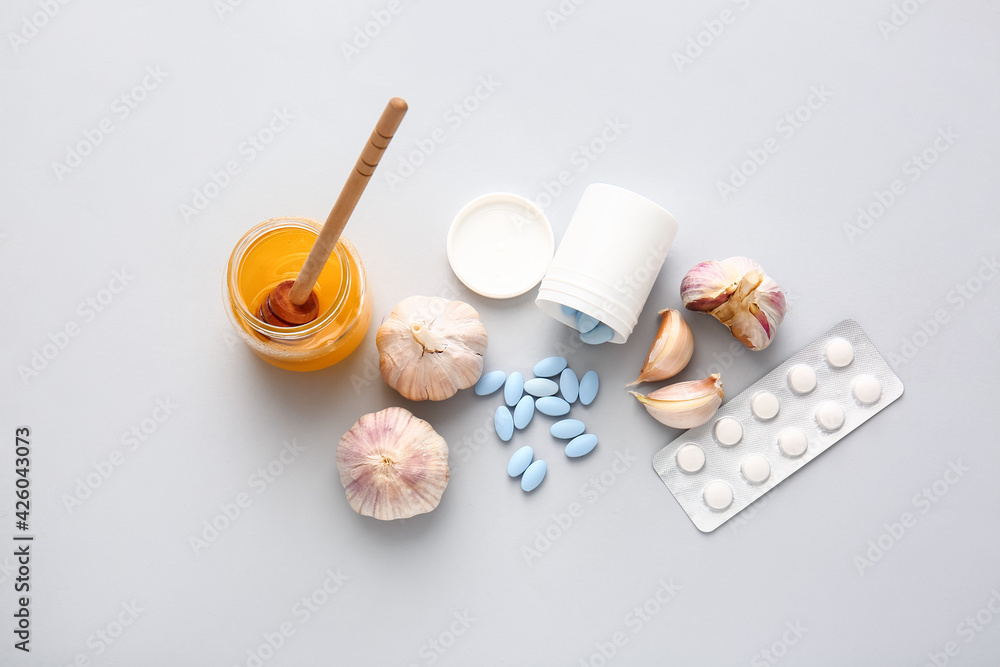Fresh garlic with honey and pills on light background Fresh garlic with honey and pills on light background