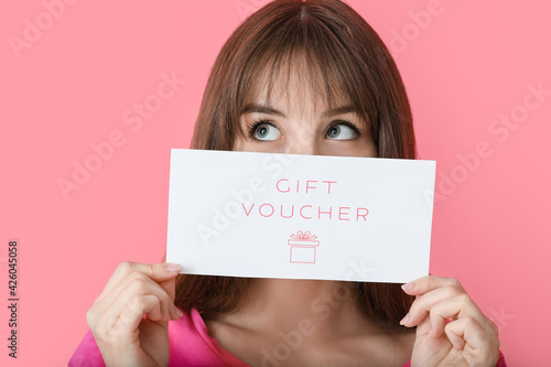 Beautiful young woman with gift voucher on color background photo