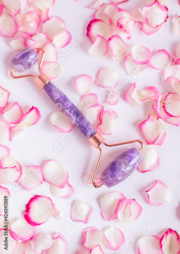 Massager roller made of amethyst on a white background with pink rose petals. Massager for lifting the skin made of natural stone.
