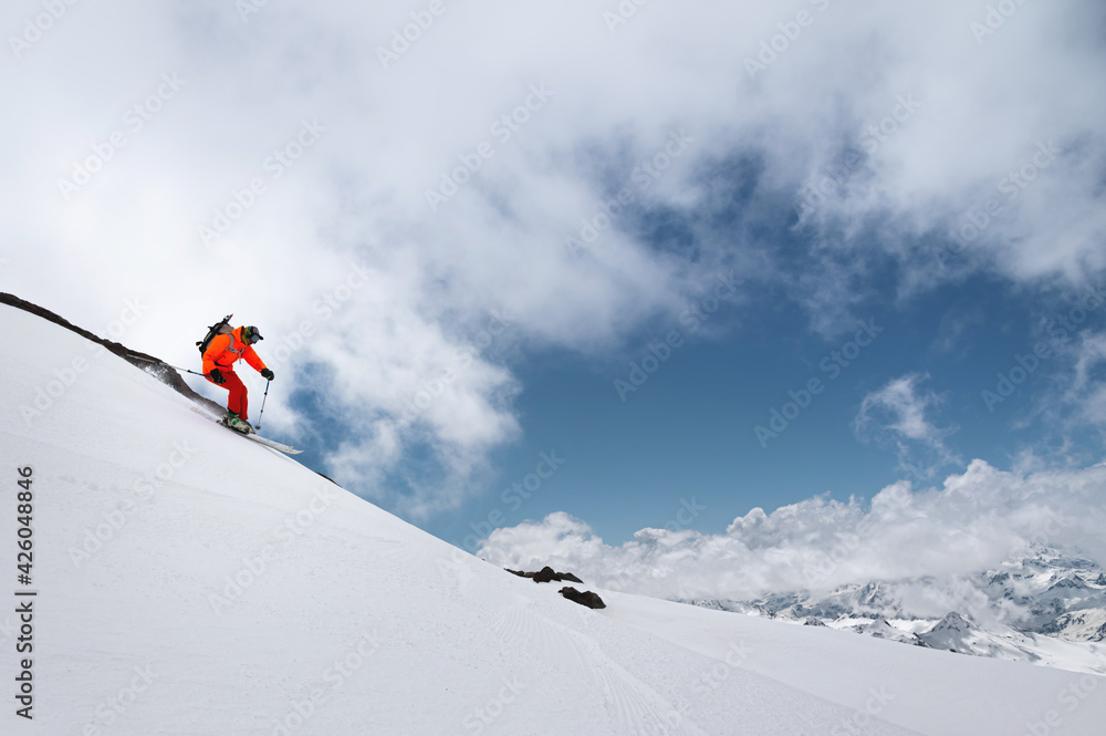 skier in bright clothes quickly descends the mountain through the snow