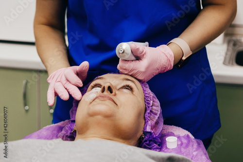 Cosmetologist is applying cream with anesthesia on patient's face, portrait closeup view.