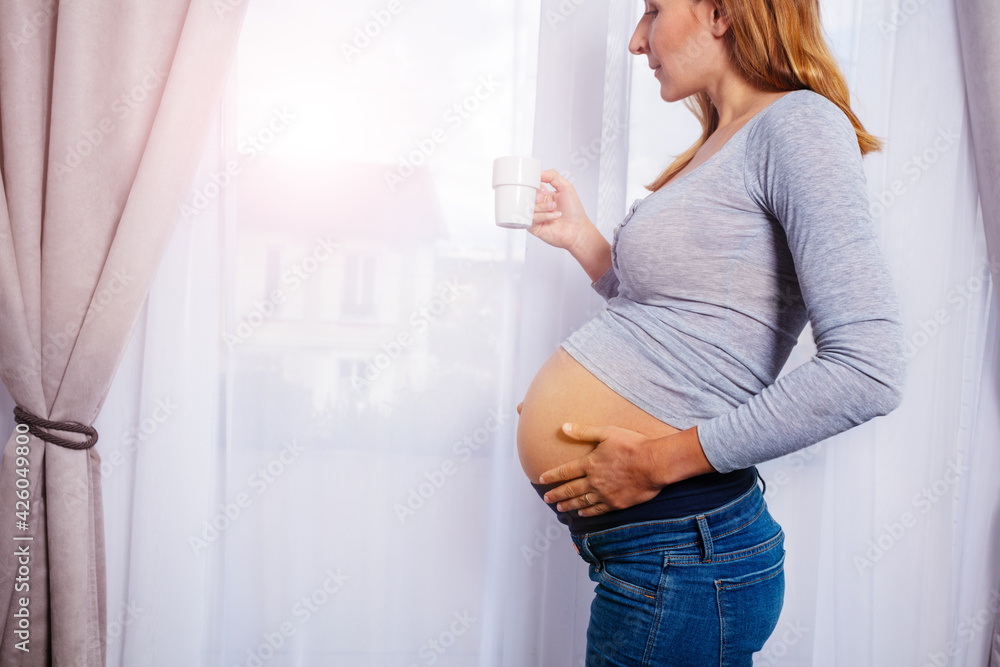 Pregnant woman drink coffee stand by the window Pregnant woman drink coffee stand by the window