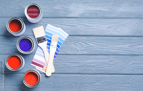 Cans of paints, brushes and palette samples on color wooden background
