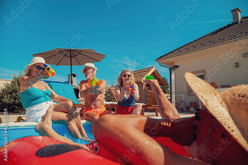 Senior friends playing with squirt guns at the swimming pool