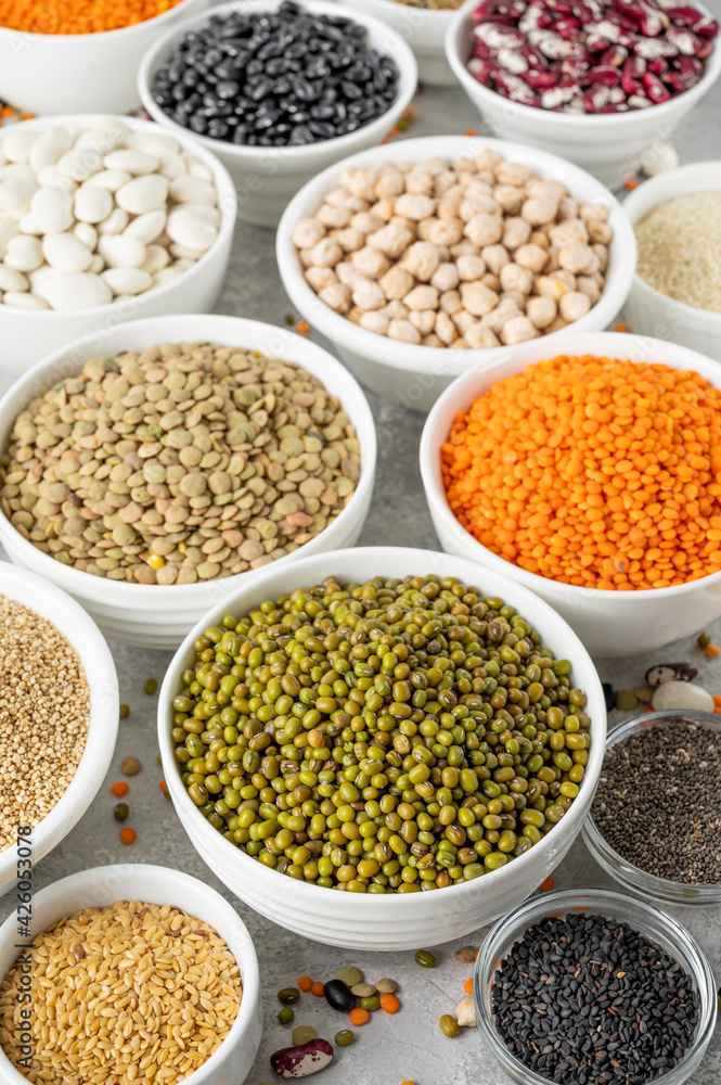 Mix of legumes, chickpeas, lentils, beans, peas, quinoa, sesame, chia, flax seeds in bowls on a gray concrete background. Healthy, vegan and gluten free food.