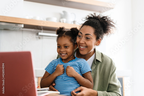 Black smiling woman making fun with her daughter while using laptop © Drobot Dean