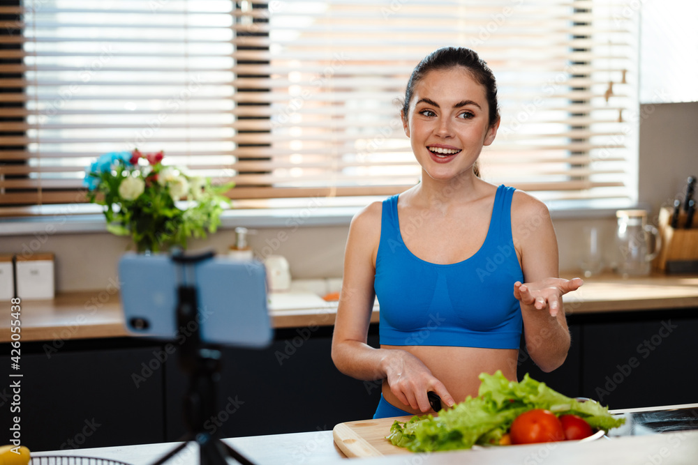 White young woman preparing salad while taking selfie footage