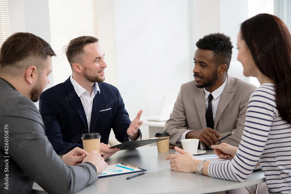 Group of multi-ethnic business people sitting around the office desk and discussing the project Group of multi-ethnic business people sitting around the office desk and discussing the project