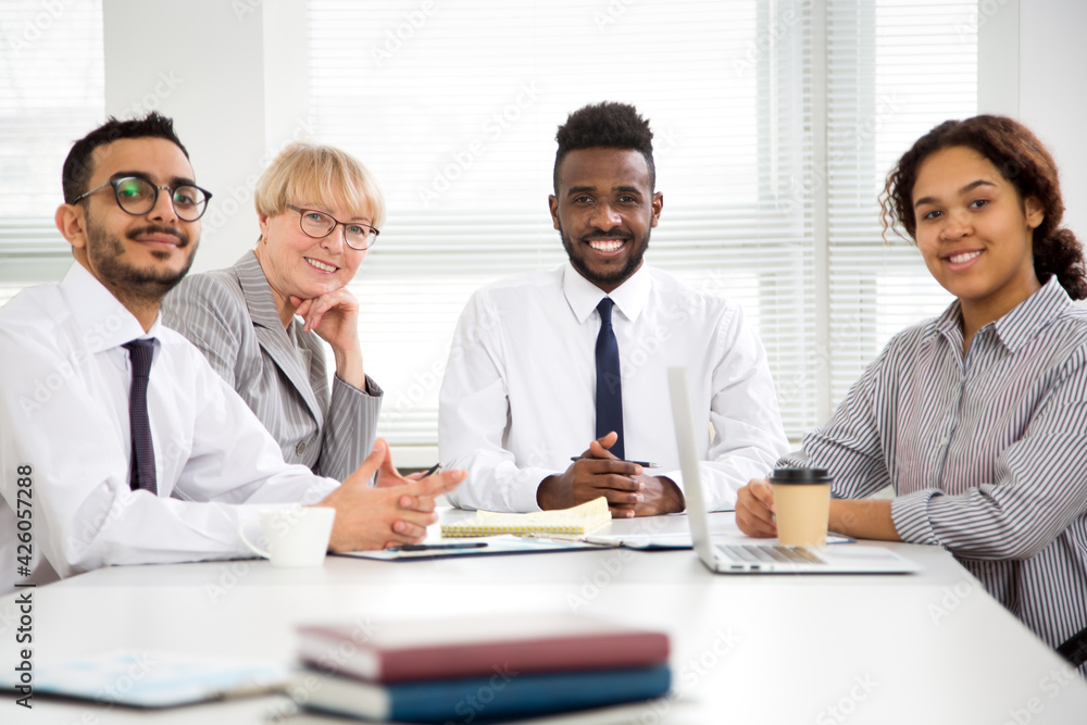 Multy-ethnic group of business people working while sitting at the office desk and smiling at camera Multy-ethnic group of business people working while sitting at the office desk and smiling at camera