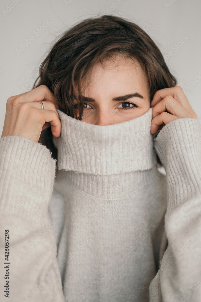 Vertical frame of a beautiful brunette. A cozy photo of a girl in a gray sweater. The girl covers her face with a jacket. Close up of a girl's eyes Vertical frame of a beautiful brunette. A cozy photo of a girl in a gray sweater. The girl covers her face with a jacket. Close up of a girl's eyes