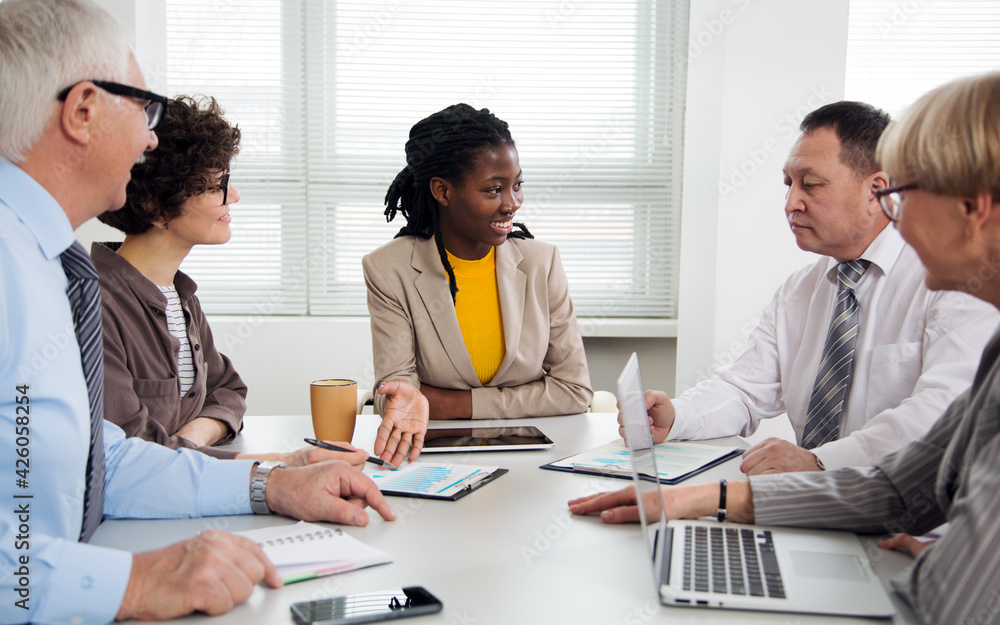 Group of multi-ethnic business people sitting around the office desk and discussing the project Group of multi-ethnic business people sitting around the office desk and discussing the project
