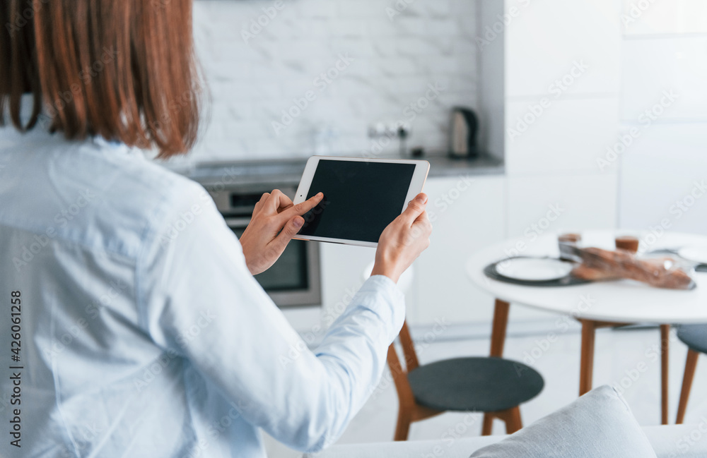 Digital tablet in hands. Young woman is indoors in smart house room at daytime Digital tablet in hands. Young woman is indoors in smart house room at daytime