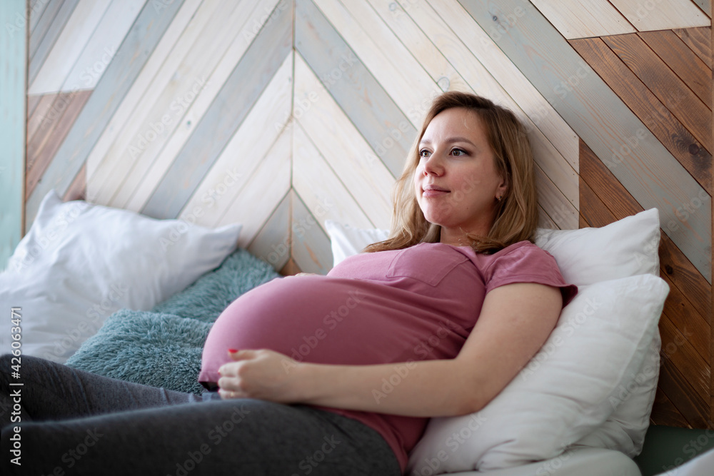 Attractive pregnant woman is sitting in bed and holding her belly. Last months of pregnancy. Attractive pregnant woman is sitting in bed and holding her belly. Last months of pregnancy.