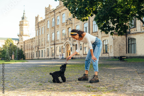 Happy woman sitting with a young little dog on the street, owner looks at the dog and smiles. Lady spends the weekend with her favorite dog, she is happy.