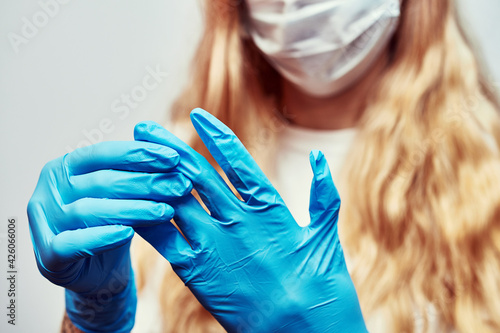 girl with blonde hair puts blue latex gloves on her hands