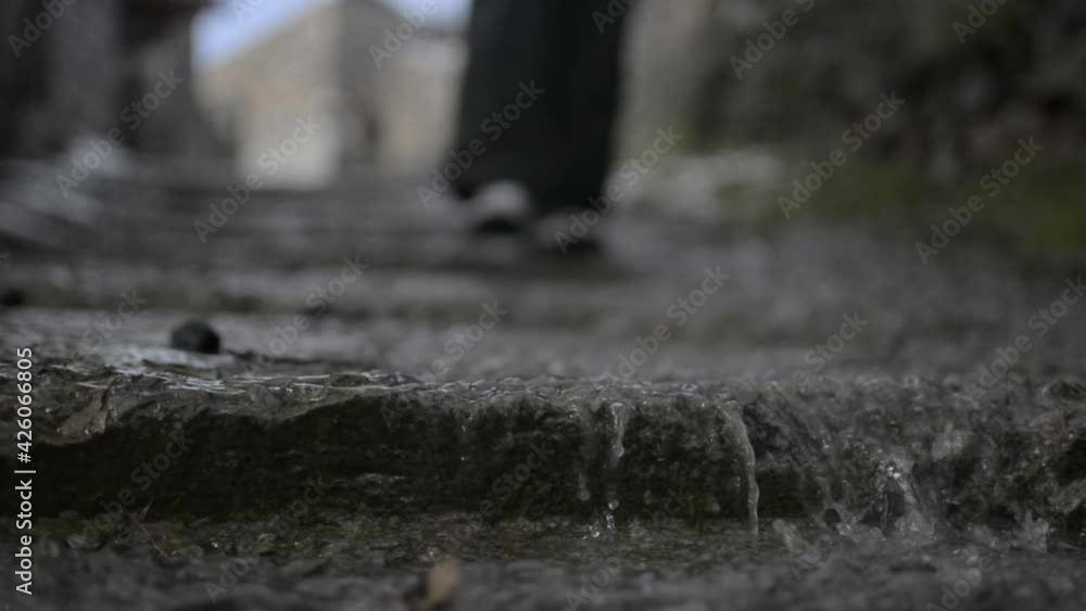 Rainwater falls down stone stairs, while a person walks down them Rainwater falls down stone stairs, while a person walks down them