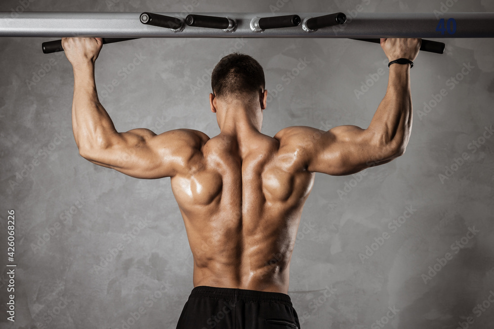 Fitness in gym, sport and healthy lifestyle concept. Handsome athletic man with naked torso making exercises. Bodybuilder male model pumping up muscles making pulls up on the crossbar. Back view Fitness in gym, sport and healthy lifestyle concept. Handsome athletic man with naked torso making exercises. Bodybuilder male model pumping up muscles making pulls up on the crossbar. Back view