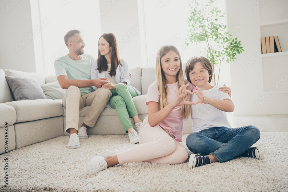 Full size photo of optimistic family mom dad two kids show heart hug sit on floor sofa wear t-shirts trousers at home Full size photo of optimistic family mom dad two kids show heart hug sit on floor sofa wear t-shirts trousers at home