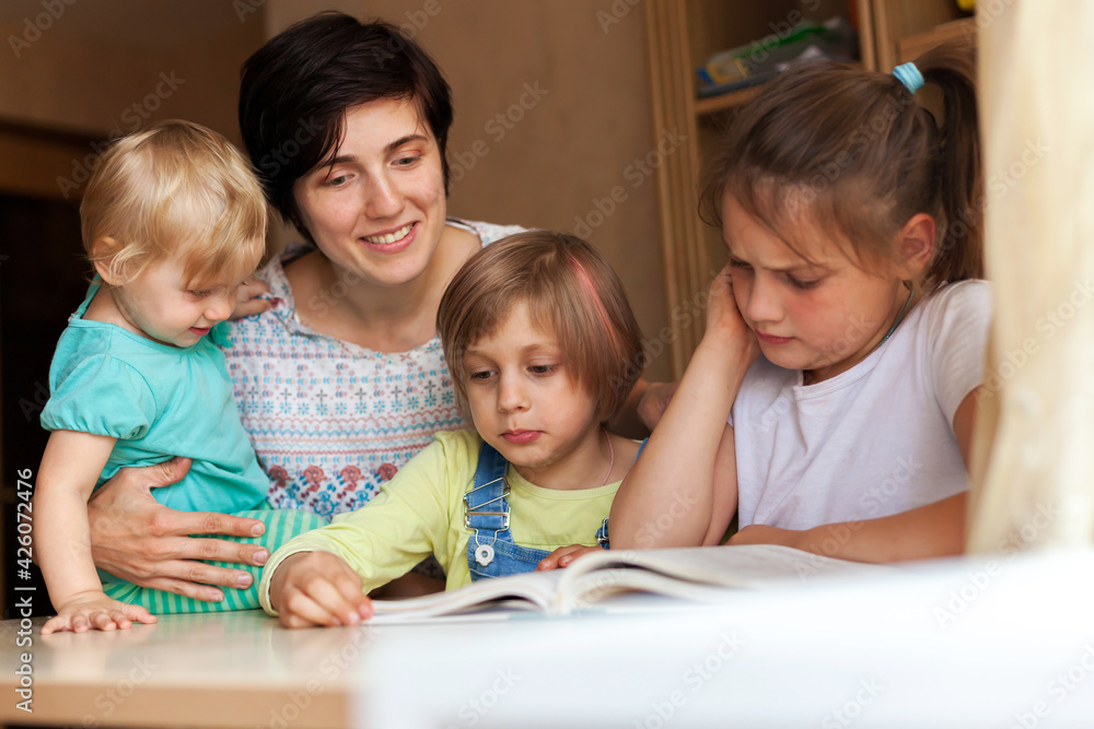 Woman with three children at table reading book Woman with three children at table reading book