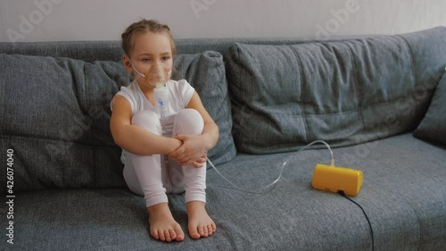 Little girl makes inhalation with medical nebulizer while sitting on bed