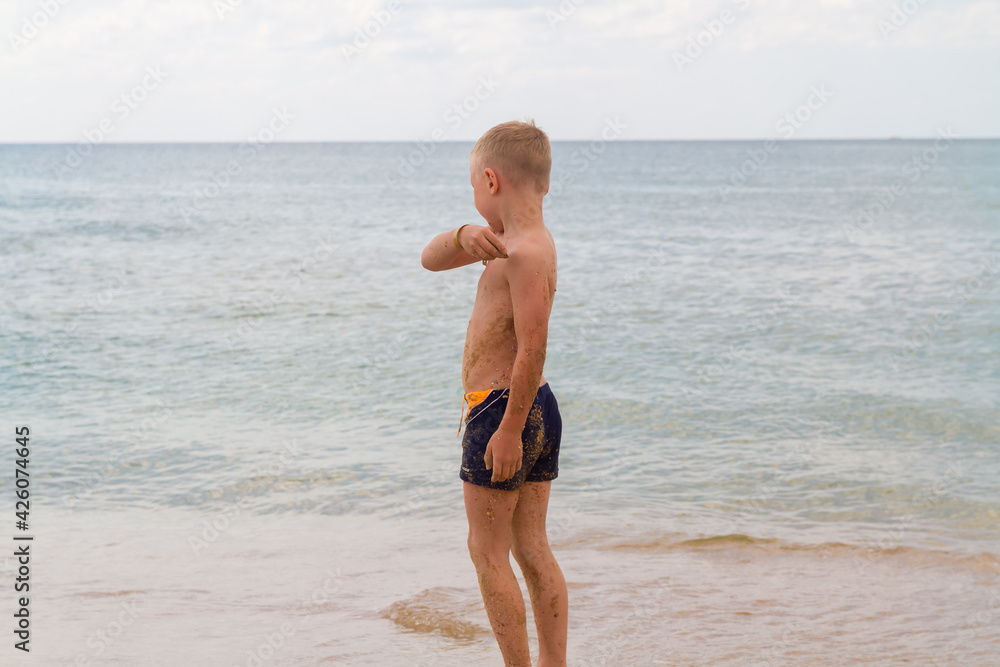 A Caucasian boy stands on the beach in summer and throws pebbles into the ocean