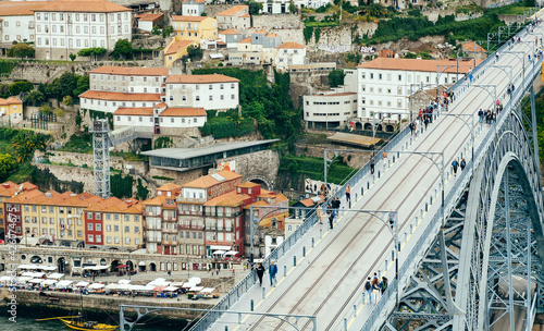 Top view on iron bridge and pedestrians walking over red tile roofs of historical buildings. Porto.