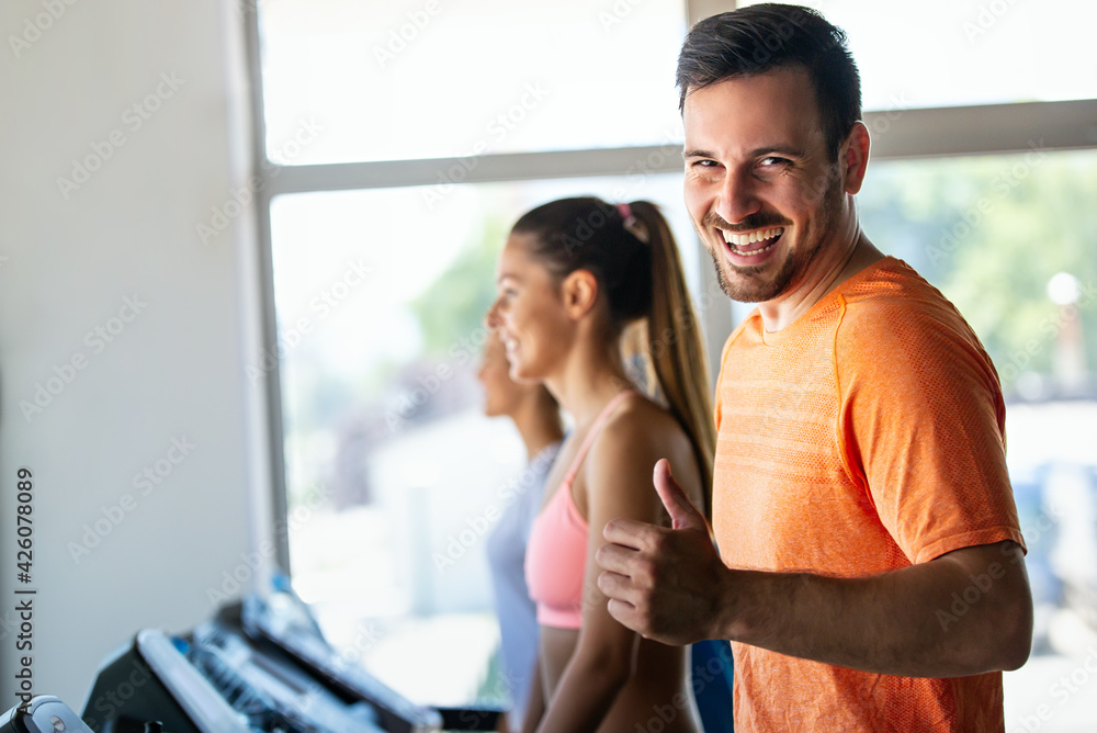 Group of happy fit young people running on a treadmill in health club Group of happy fit young people running on a treadmill in health club