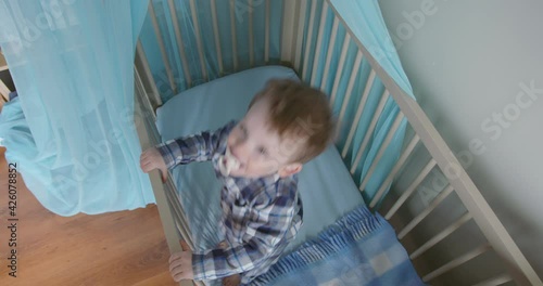 Baby boy having fun jumping up and down in his crib, topview slow motion