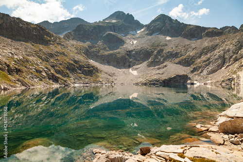 Landscape photograph of a lake with clean and turquoise waters that reflect the silent silhouettes of the mountains in summer, Aragonese Pyrenees, Huesca province, Posets-Maladeta Natural Park.
