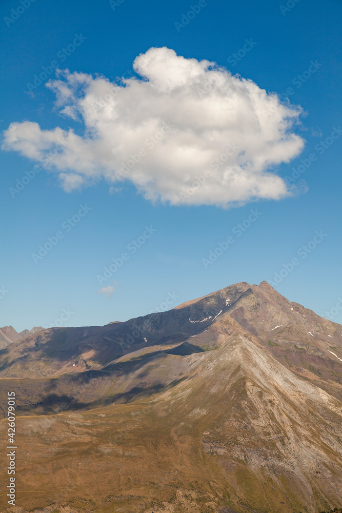 Landscape photography of steep mountains in summer, lonely clouds, and silent high altitude pastures, in the Aragonese Pyrenees, Huesca province, in the area of the Posets-Maladeta Natural Park.