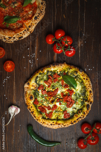 Homemade pizza with spinach, dried tomatoes and pine nuts. Overhead, dark wooden background, vertical