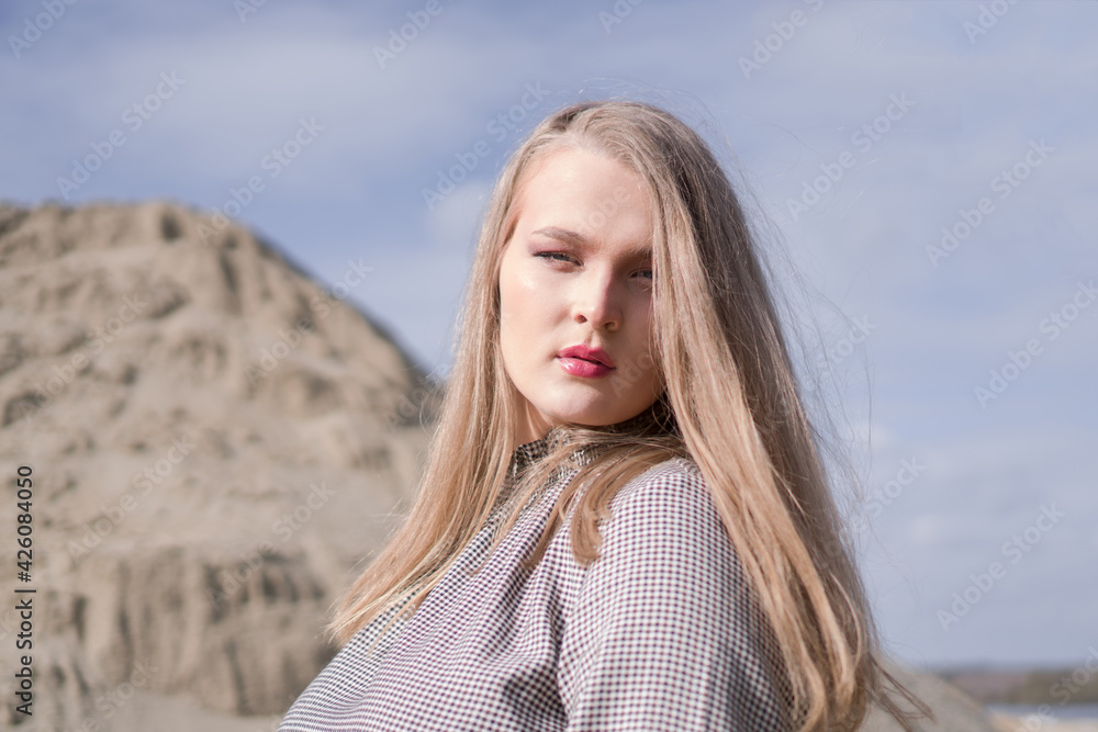 Beauty portrait of a young blond girl in a vintage dress. She is posing on a sandy landscape.