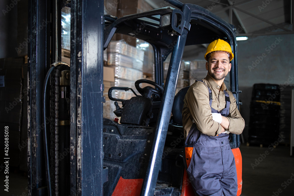 Portrait of warehouse forklift driver standing in storehouse by the machine. Portrait of warehouse forklift driver standing in storehouse by the machine.