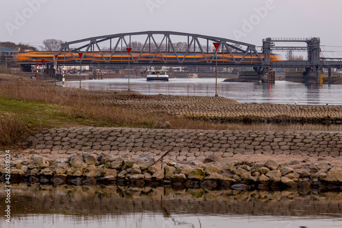 Steel construction draw bridge over river IJssel with a Dutch railways train passing over it city of Zutphen in the back and cargo ship beneath