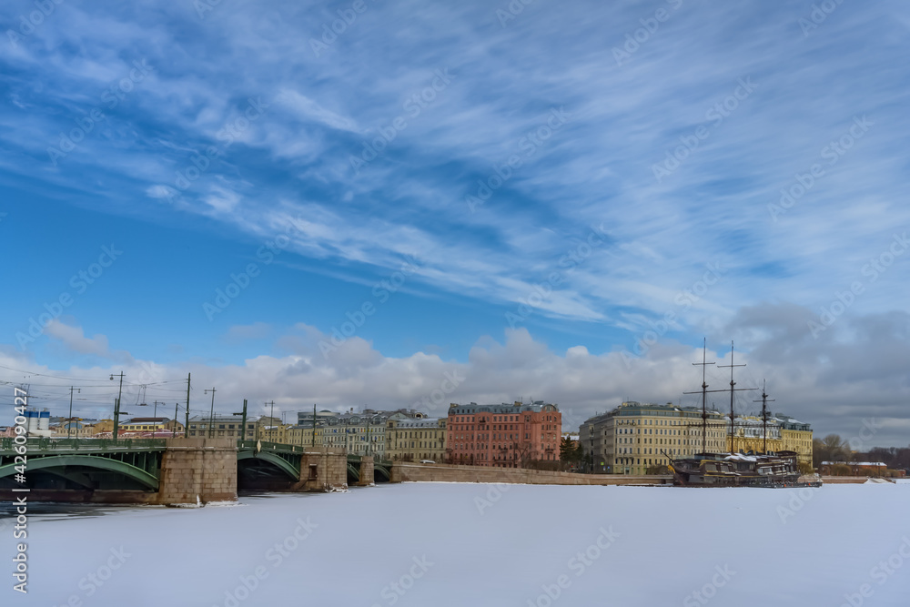 Naklejka premium View of the city of St. Petersburg (Russia) on a sunny day in early spring with its bridges across the rivers, old historical houses and an old ship frozen in ice. Beautiful deep blue sky