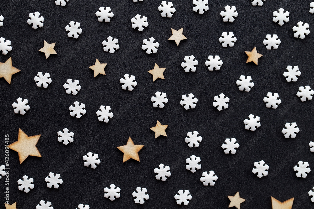 Small white snowflakes and wooden stars on a dark acrylic background taken close up Small white snowflakes and wooden stars on a dark acrylic background taken close up